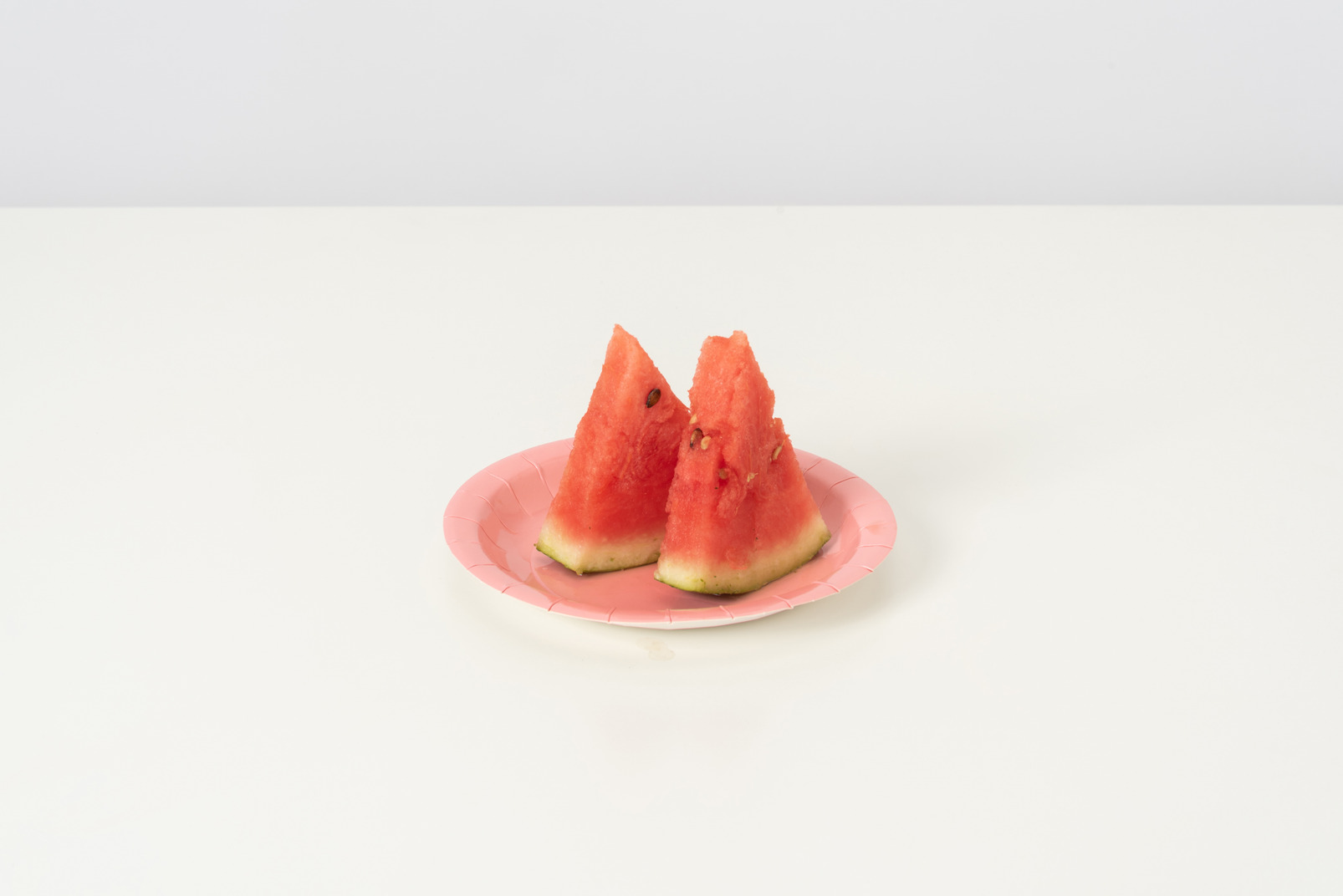 Two slices of a sweet ripe watermelon, lying isolated against a white background on a cute pink plate