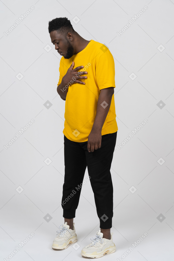 Vista de tres cuartos de un joven sorprendido de piel oscura con camiseta amarilla tocando el pecho