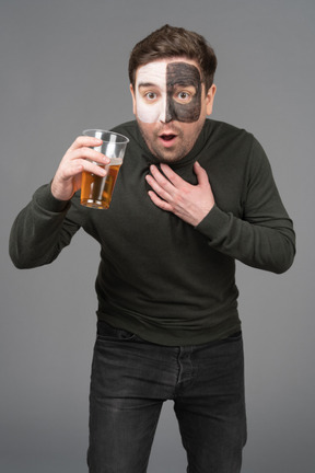 Vista frontal de un fanático del fútbol masculino sorprendido sosteniendo una cerveza e inclinándose hacia adelante