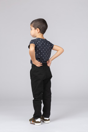 Vista trasera de un chico lindo en ropa casual posando con las manos en la espalda