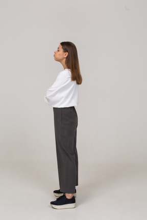 Vista laterale di una giovane donna in abiti da ufficio che soffia sulle guance e incrocia le braccia