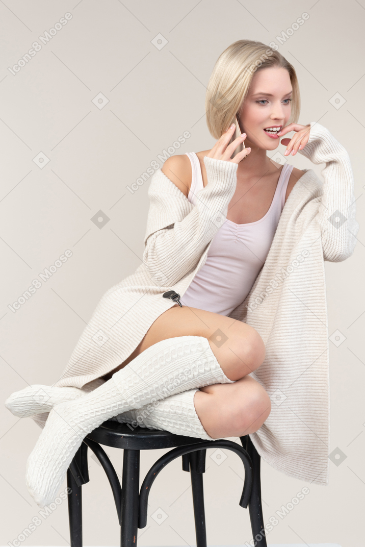 Songeuse jeune femme assise sur une chaise et parlant au téléphone