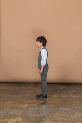 Boy in grey suit standing in profile and making faces