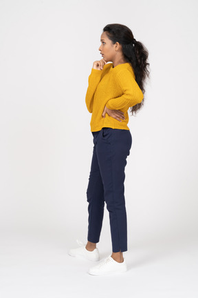 Vista lateral de uma garota pensativa em roupas casuais, posando com a mão no quadril