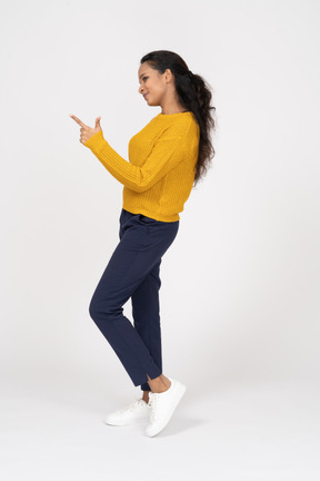 Vista lateral de uma garota com roupas casuais apontando com o dedo