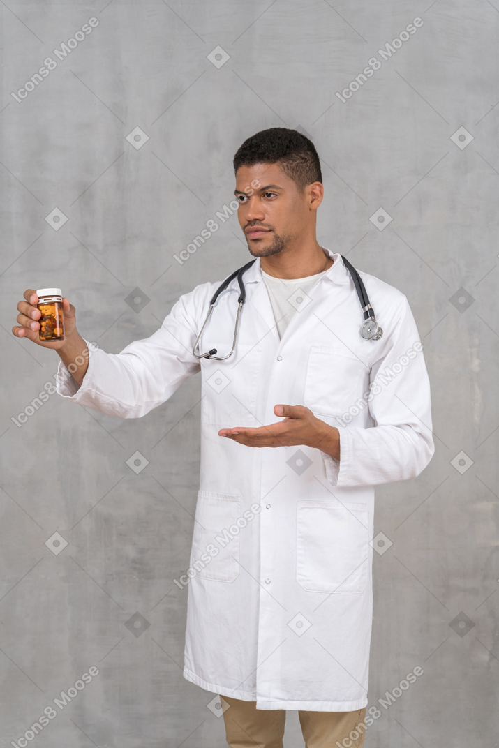 Молодой врач показывает пузырек с таблетками