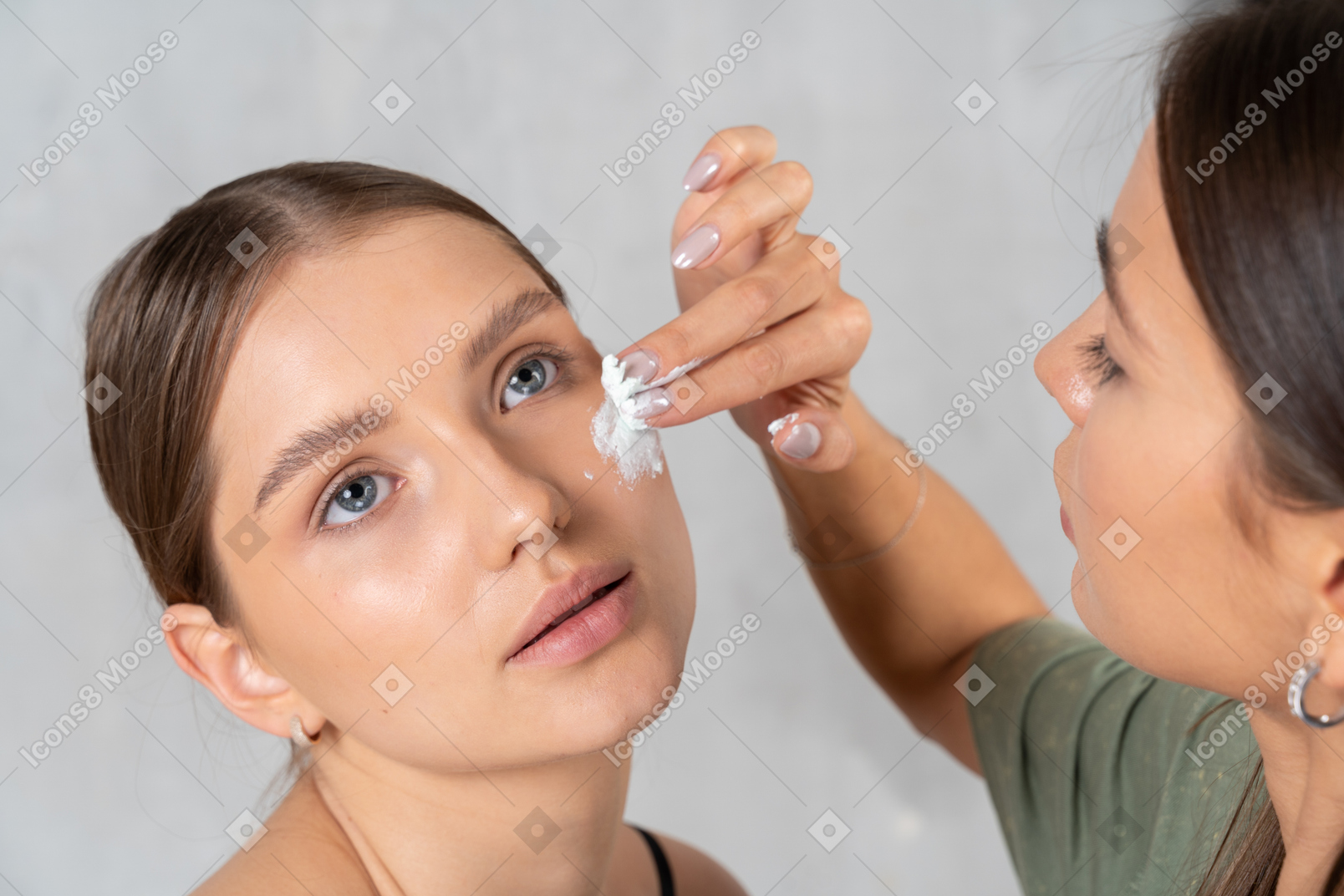 Beautician applying face cream on young woman's face