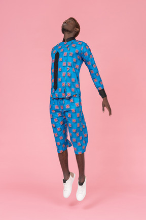 Black man in blue pajamas jumping on pink background