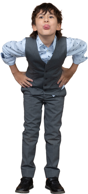 Front view of a boy in grey suit posing with hands on hips and showin tongue