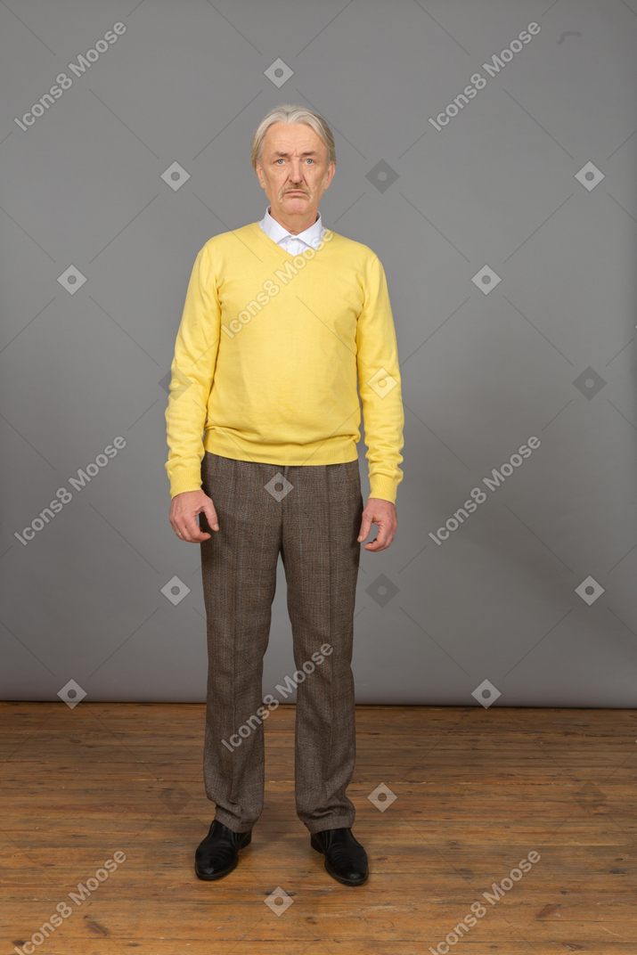 一个不高兴的老人穿着黄色套头衫，看着相机的前视图
