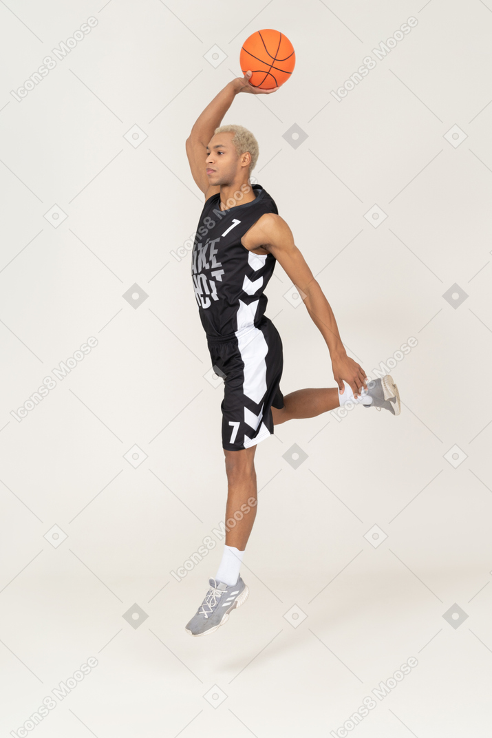 Vista lateral de um jovem jogador de basquete marcando um ponto