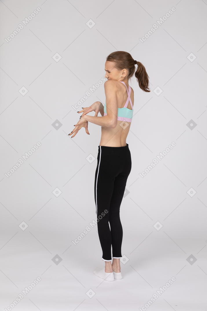 Vista posterior de tres cuartos de una jovencita disgustada en ropa deportiva entrecerrando los ojos y gesticulando
