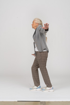 Side view of an old lady in suit balancing with outstretched arms