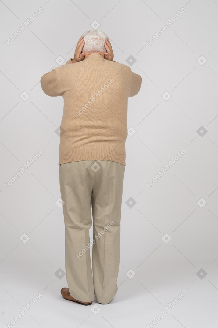 手で耳を覆うカジュアルな服を着た老人の背面図