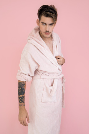 Handsome young guy standing in pink robe and watching to the camera closely