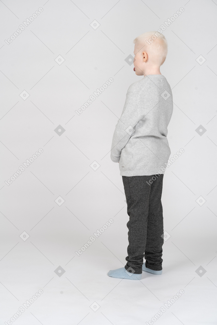 Back three-quarter view of a kid boy in casual clothes showing tongue