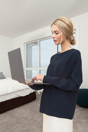 A woman standing in a bedroom using a laptop computer