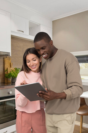 A man and a woman standing in a kitchen looking at a tablet