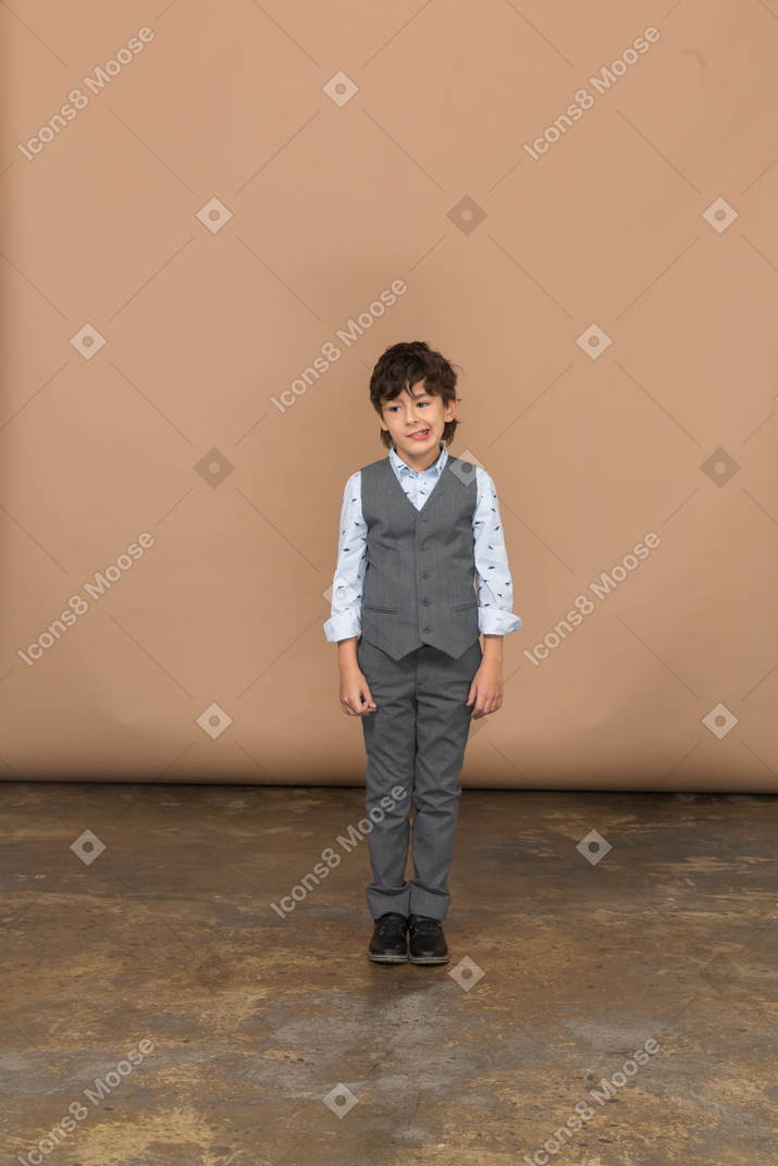 Vista frontal de un chico lindo en traje mirando a la cámara y haciendo muecas