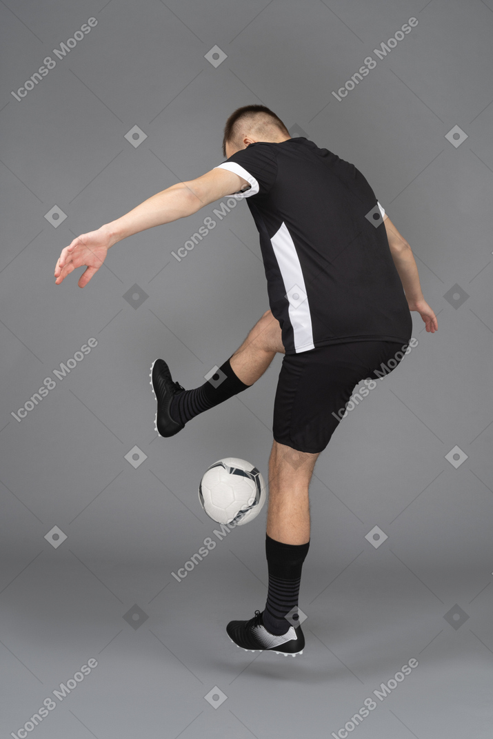 Три четверти сзади мужского футболиста, поднимающего руки и выполняющего трюк