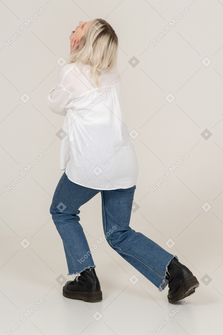 Three-quarter back view of an exhausted blond female touching face and stepping aside