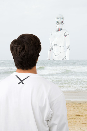 A man is looking at a robot on the beach