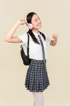 亚洲学校的女孩在耳机听音乐闭着眼睛，跳舞