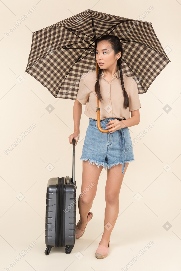 Mulher jovem séria com mala e guarda-chuva olhando de lado