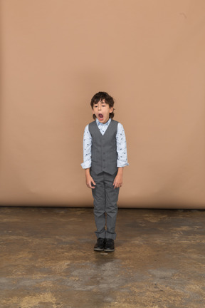 Vista frontal de un niño en traje mirando a la cámara y bostezando