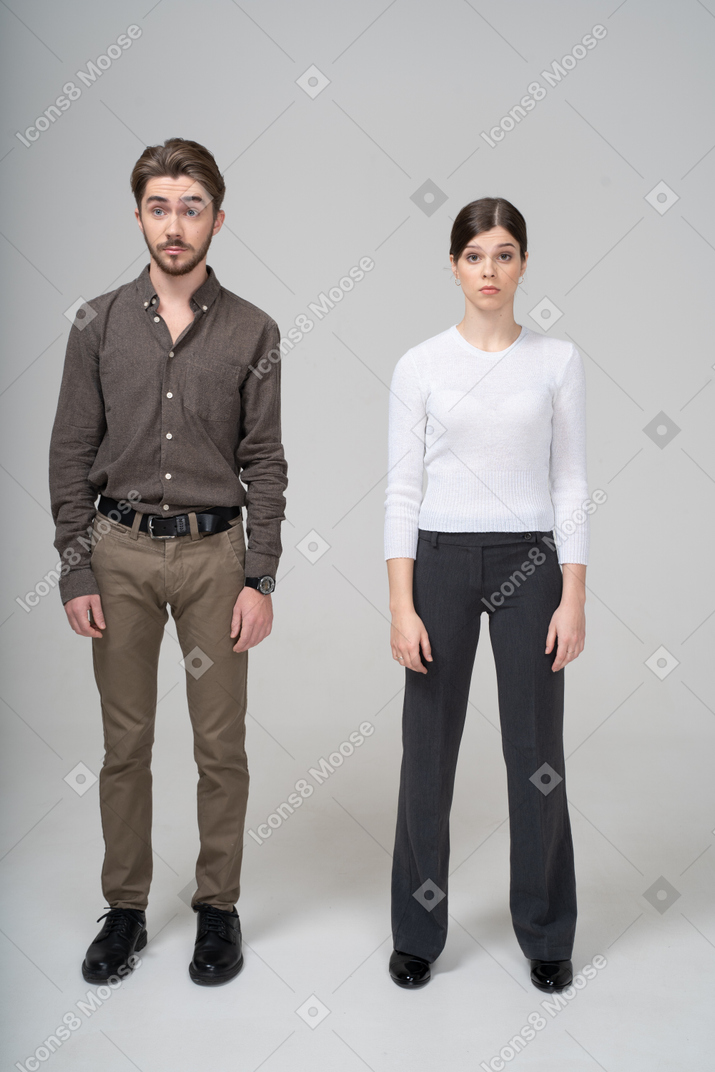 Vista frontal de una joven pareja sorprendida en ropa de oficina levantando las cejas