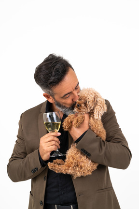 Reifer mann, der ein glas wein hält und einen welpen küsst