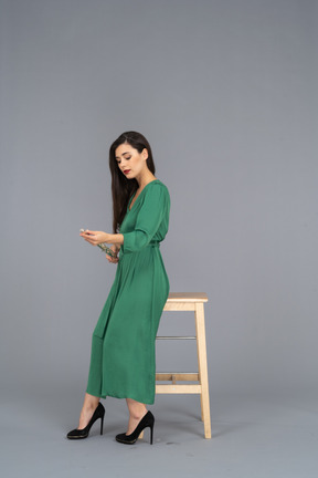 Вид сбоку молодой леди в зеленом платье, сидящей на стуле и держащей кларнет