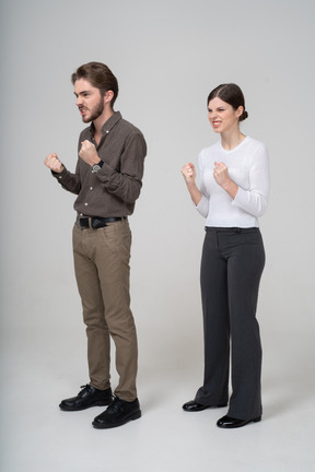 Vue de trois quarts d'un couple furieux en vêtements de bureau serrant les poings