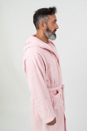 Зрелый мужчина в розовом халате стоит в профиль