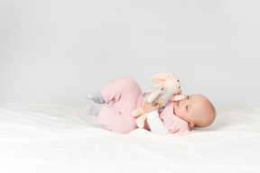 女婴躺在背上，抱着毛绒的玩具