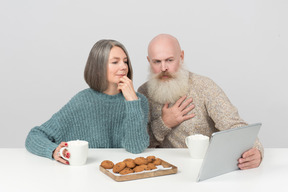 年长的夫妇在平板电脑上喝咖啡和看电影