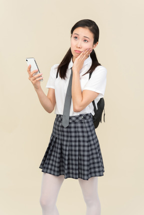 Pensive asian school girl looking at phone