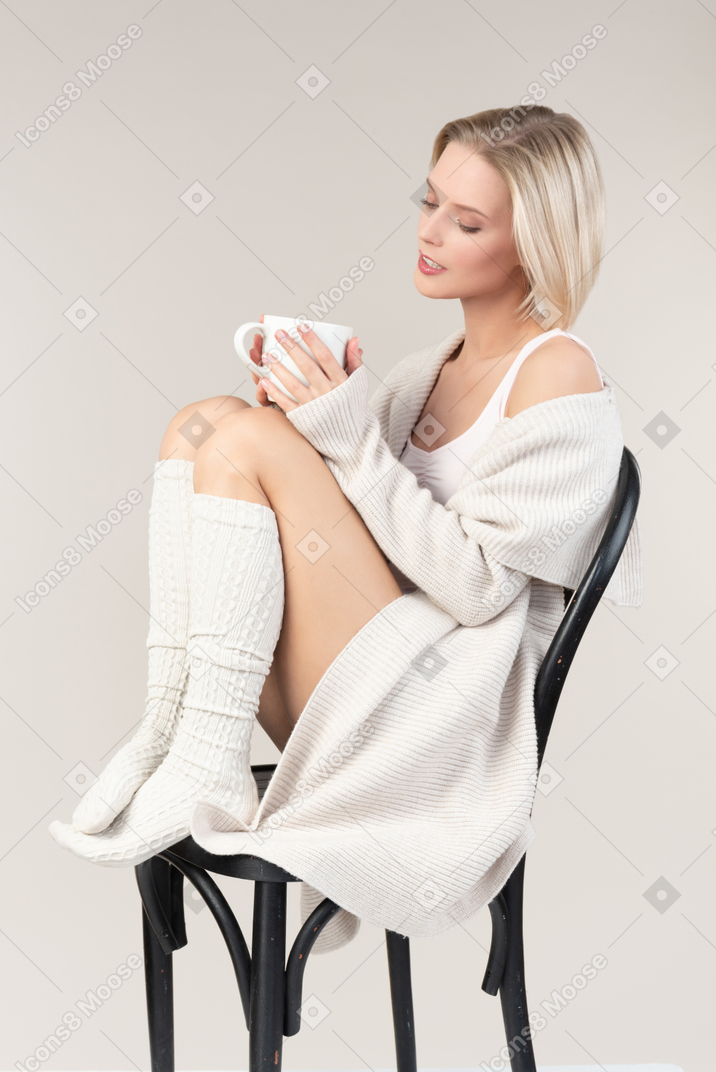Dreamy young woman holding cup and sitting on chair