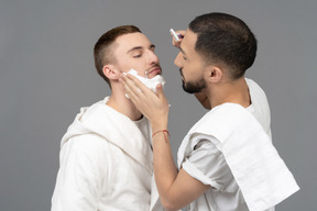 Junger kaukasischer mann, der seinen partner sorgfältig rasiert und seine wange berührt