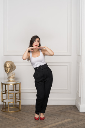 Front view of a cute young female putting hands under chin while standing near golden greek sculpture