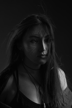 Close-up dark silhouette of a young female with face art  and messy hair looking aside