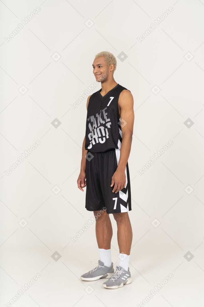 Vista di tre quarti di un giovane giocatore di basket maschile sorridente in piedi immobile