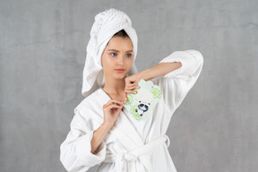Mujer en bata de baño abriendo un paquete de máscara de hoja