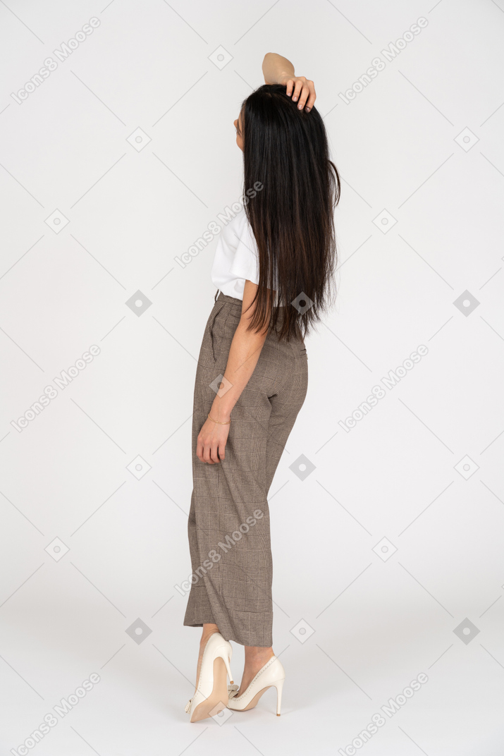 Vista posterior de tres cuartos de una mujer joven en calzones tocando la cabeza