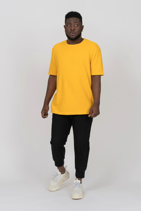 Vista frontal de un desconcertado joven de piel oscura con camiseta amarilla mirando a un lado