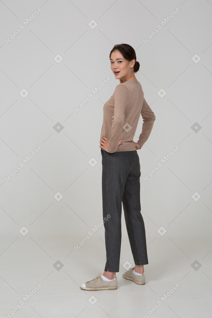 Vista posteriore di tre quarti di una giovane donna in pullover beige che mette le mani sui fianchi