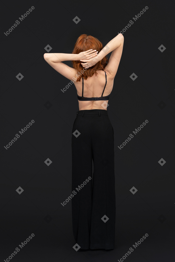 A back side view of the pensive beautiful woman posing on the black background holding her hand on the head