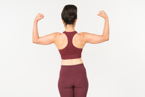 Young indian woman in sportswear showing muscles and standing back to camera