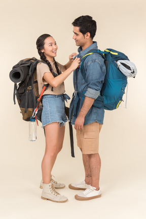 Riendo joven pareja interracial de pie cerca uno del otro con mochilas