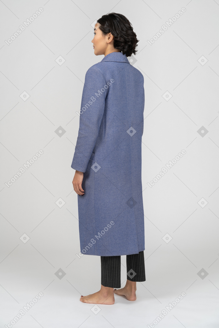 Rückansicht einer frau in blauem mantel, die mit den armen an den seiten steht